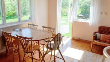 Un comedor con una mesa y sillas de madera, ventanas grandes con cortinas y vistas a la vegetación.