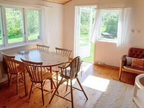 A dining area with a wooden table and chairs, large windows with curtains, and a view of greenery outside. - 4 Person Holiday Home in Tyreso (Tyreso)