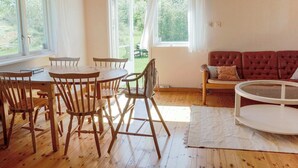 A cozy room with a wooden dining table and chairs, a red sofa, and a glass coffee table. There are large windows providing natural light and a view of greenery outside. - 4 Person Holiday Home in Tyreso (Tyreso)