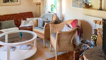 Una sala de estar acogedora con un sofá de cuero marrón, sillas de mimbre, una mesa de centro blanca y una chimenea con objetos decorativos.