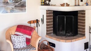 A cozy living room with a wicker armchair, a fireplace, and a basket of firewood. - 4 Person Holiday Home in Tyreso (Tyreso)