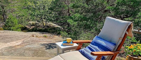 Une terrasse en bois avec un fauteuil de relaxation et une petite table sur laquelle se trouvent un livre et un bol.