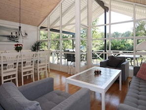A spacious room with a high ceiling, large windows, a dining area with white furniture, and a seating area with grey sofas. - Holiday Home in Hadsund (Hadsund)