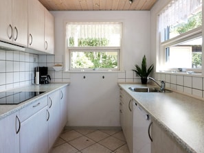 A kitchen with white cabinets, a window with a view of greenery, a sink, and a coffee maker. - Holiday Home in Hadsund (Hadsund)