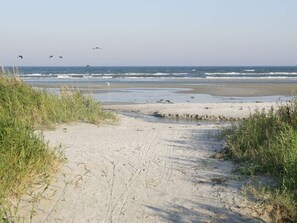 A sandy beach path leading to the ocean with waves crashing onto the shore.