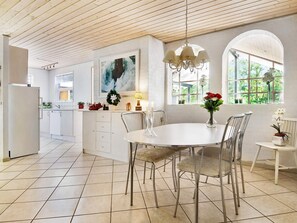 A modern kitchen with white cabinetry, a dining area with a round table and metal chairs, and a large window providing natural light.