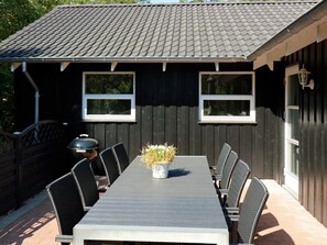 A dining area with a long table and chairs, a grill, and a potted plant.