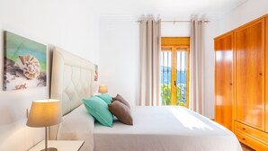 Une chambre à coucher avec un lit, une table de chevet, une lampe, une armoire et une fenêtre avec des rideaux.