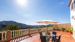 Une terrasse avec une table et des chaises, un grand parasol et des plantes en pot.