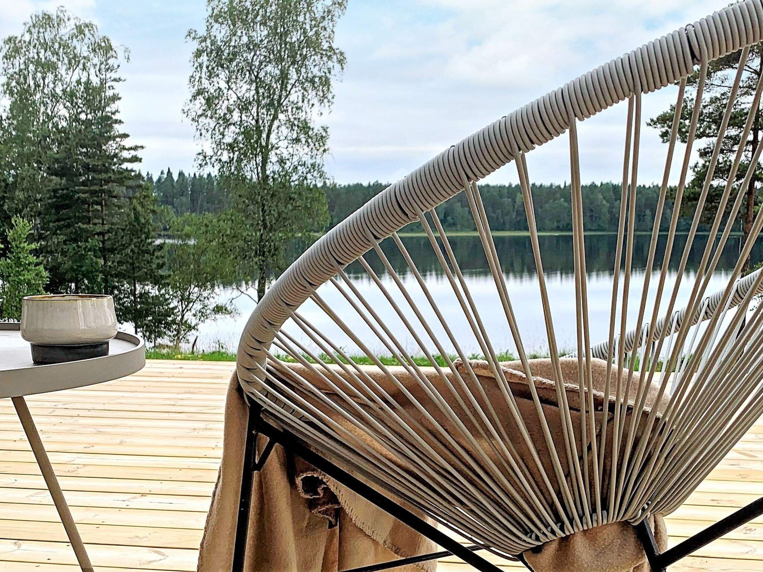 A wicker chair with a view of a lake and trees.