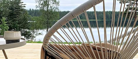 A wicker chair with a view of a lake and trees.