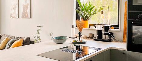 A modern kitchen with a central island, a coffee machine, and a view of the outdoors through a window.