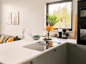 A modern kitchen with a central island, a coffee machine, and a view of the outdoors through a window.