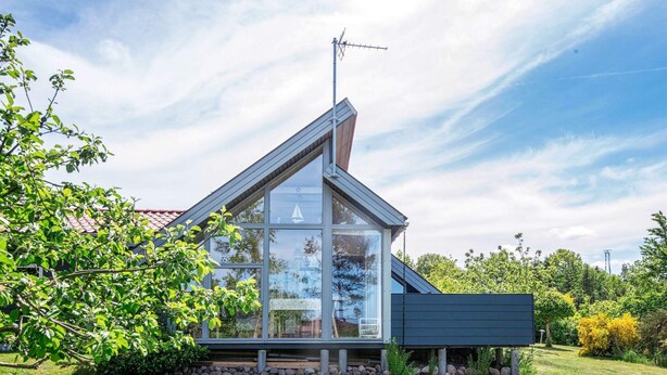 Ein modernes Haus mit großer Glasfassade, einem geneigten Dach und einer sichtbaren Antenne.