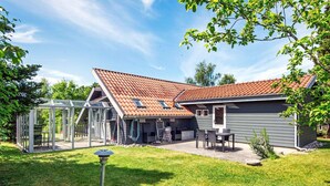 Ein Haus mit einer überdachten Terrasse, einem Grillplatz und einem eingezäunten Garten.
