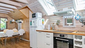 Eine kleine Küche mit Holzboden, weißen Schränken, einer Mikrowelle, einem Kühlschrank und einem eingebauten Backofen.