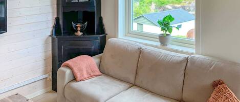 A room with a beige sofa, a dark wooden cabinet, a window with a view of greenery, and a potted plant on the windowsill.