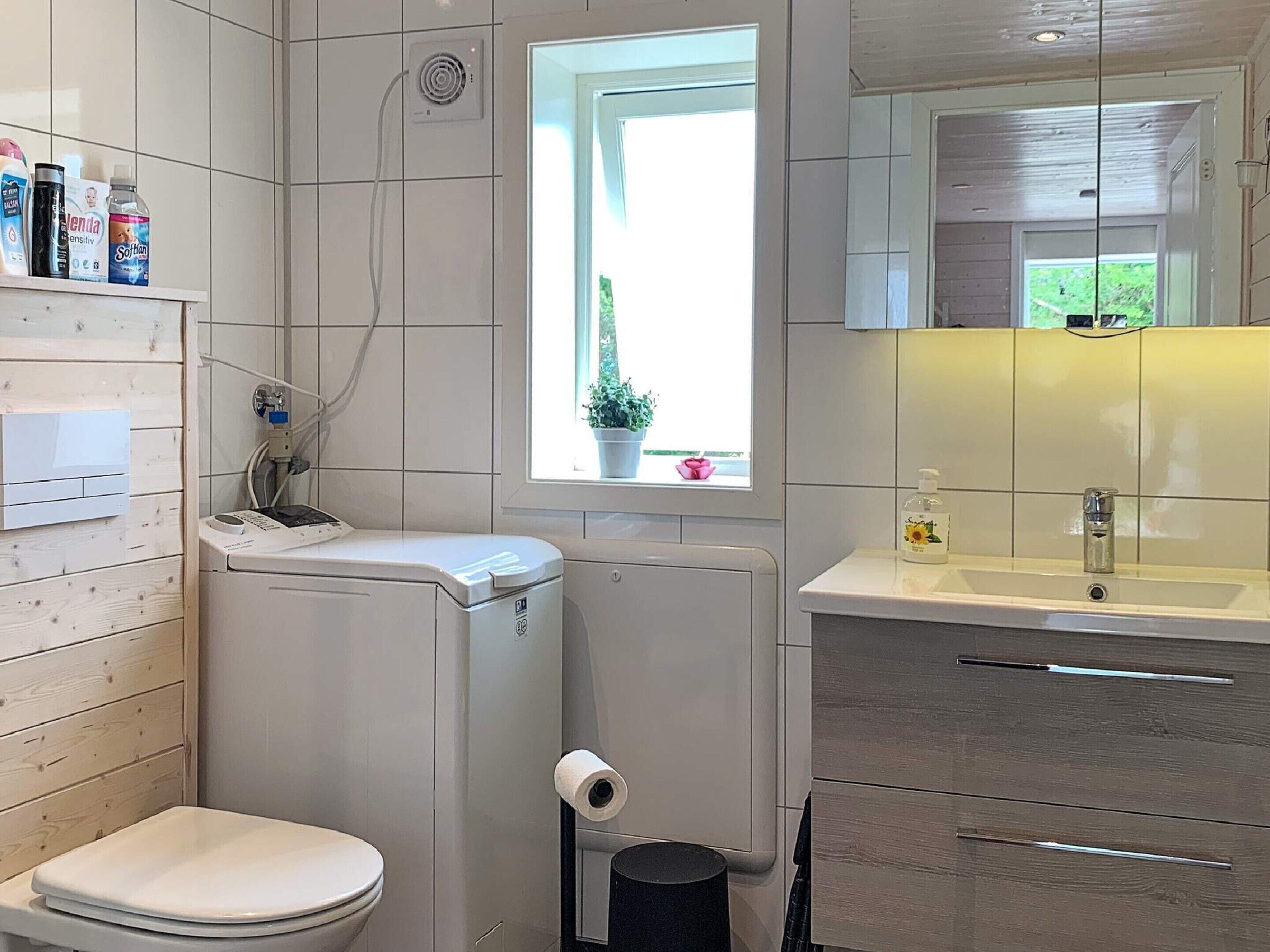 A modern bathroom with a toilet, bidet, and sink. There is a window with a view of greenery outside.