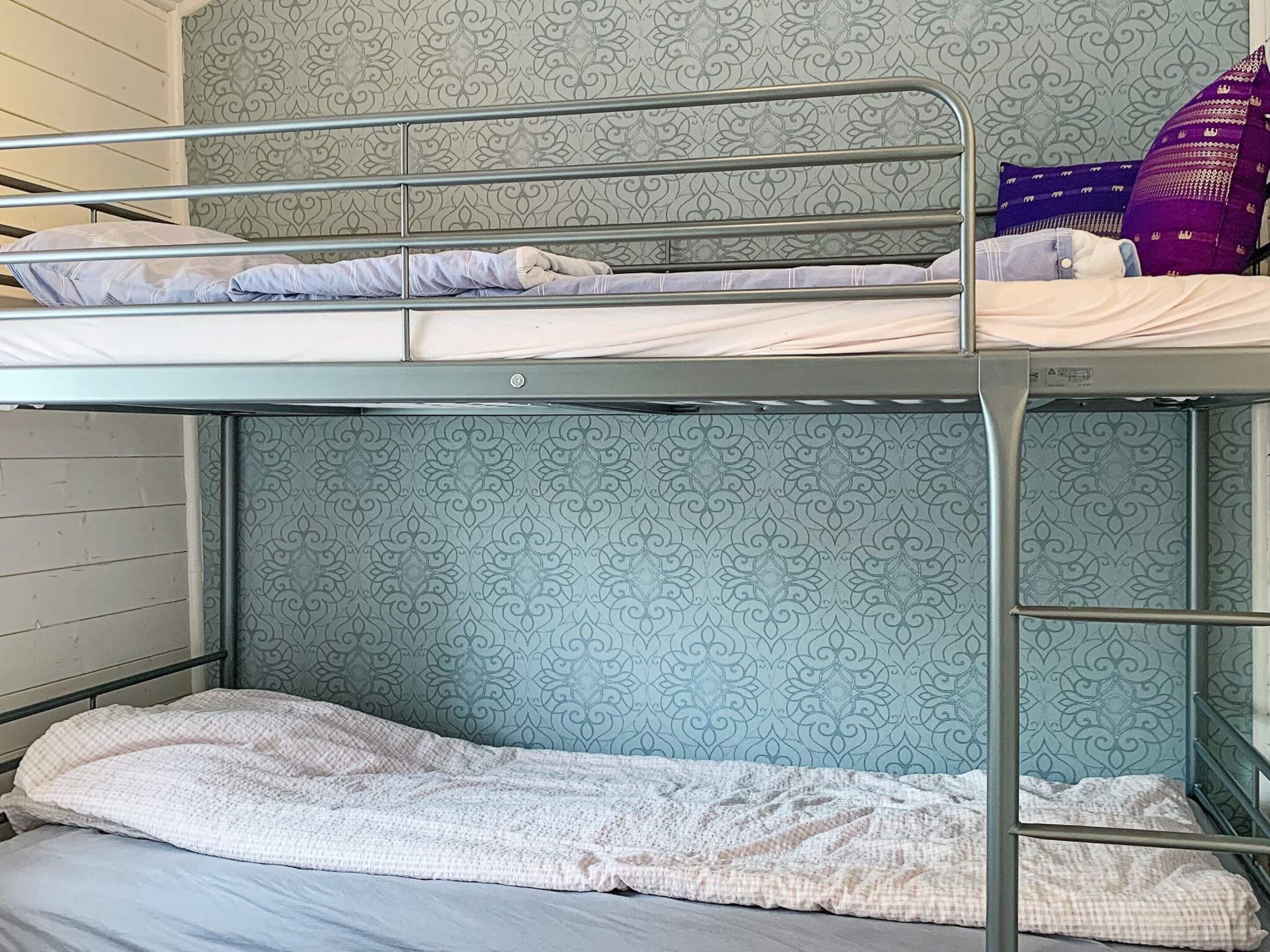 A bunk bed with patterned wallpaper, a metal frame, and pillows.