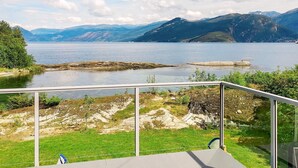 A lakeside view with mountains in the background, a grassy area, and a metal railing. - 5 Person Holiday Home in Torrvikbygd (Kvam)