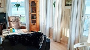 Een woonkamer met een zwarte bank, een houten kast, een bruine leren fauteuil, een houten tafel en uitzicht op de omgeving.