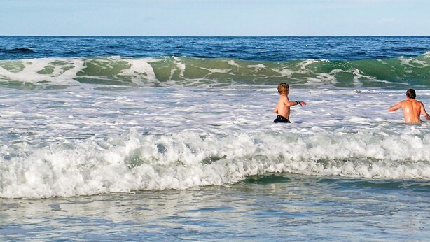 Een strandscène met golven en twee mensen in het water.