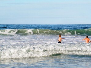 A beach scene with waves and two people in the water.