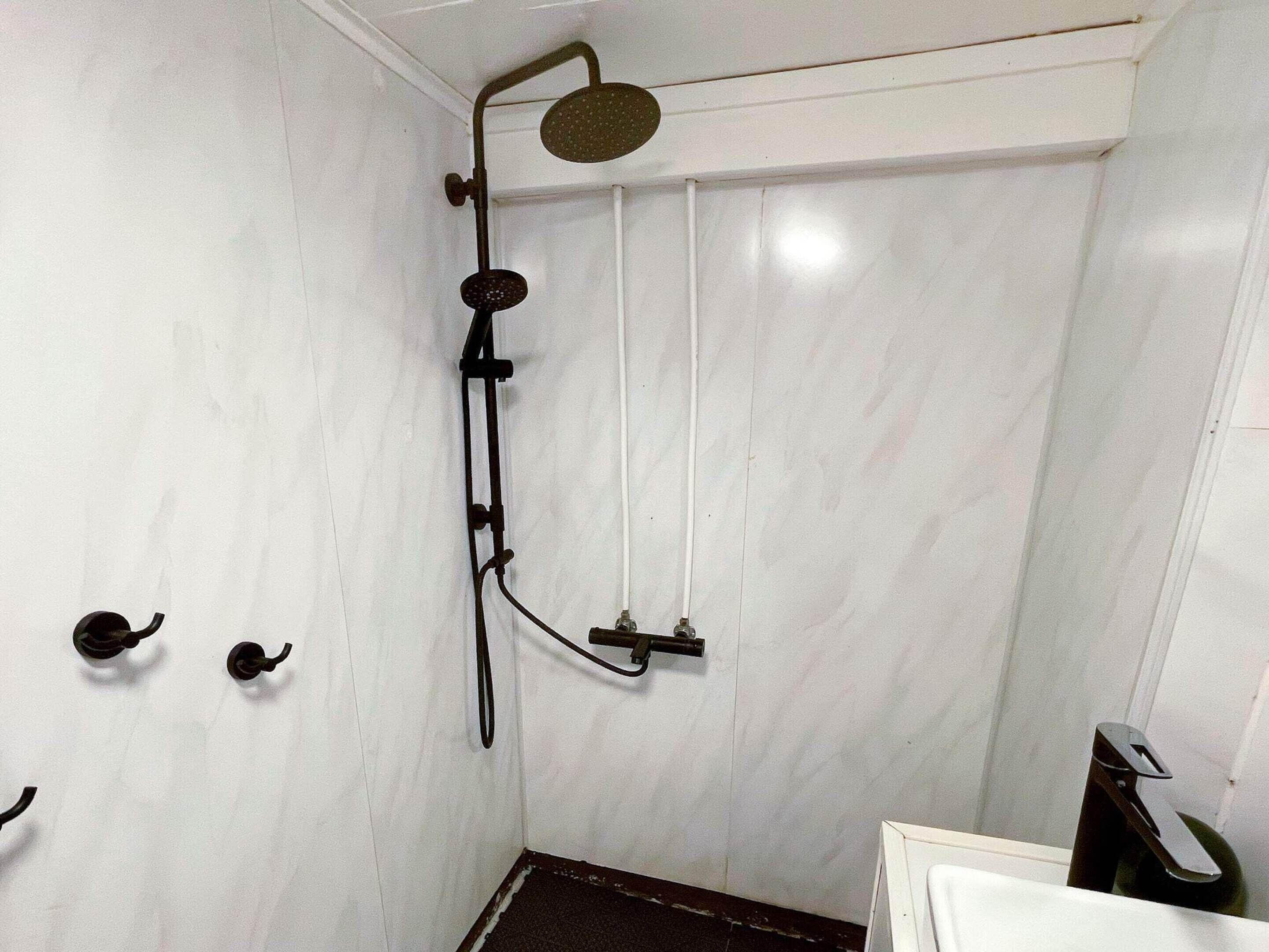 A small, enclosed shower area with a handheld showerhead and a wall-mounted faucet.