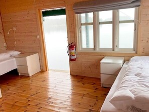 A cabin-style room with wooden walls, a wooden floor, a window with a view, a fire extinguisher, and a bed. - 6 Person Holiday Home in Lindas (Alver)