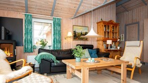 A cozy living room with a fireplace, wooden furniture, and a large painting on the wall. - Holiday Home in Rømø (Rømø)