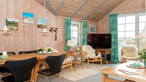 A cozy living room with wooden walls, a dining area, and a TV. - Holiday Home in Rømø (Rømø)