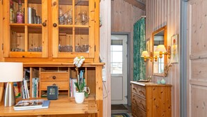 A wooden interior with a cabinet containing glassware, a small table with a plant, and a dresser with a mirror. - Holiday Home in Rømø (Rømø)