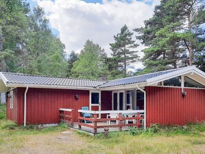 Eine rote Holzhütte mit geneigtem Dach und einer Veranda mit Sitzgelegenheiten.