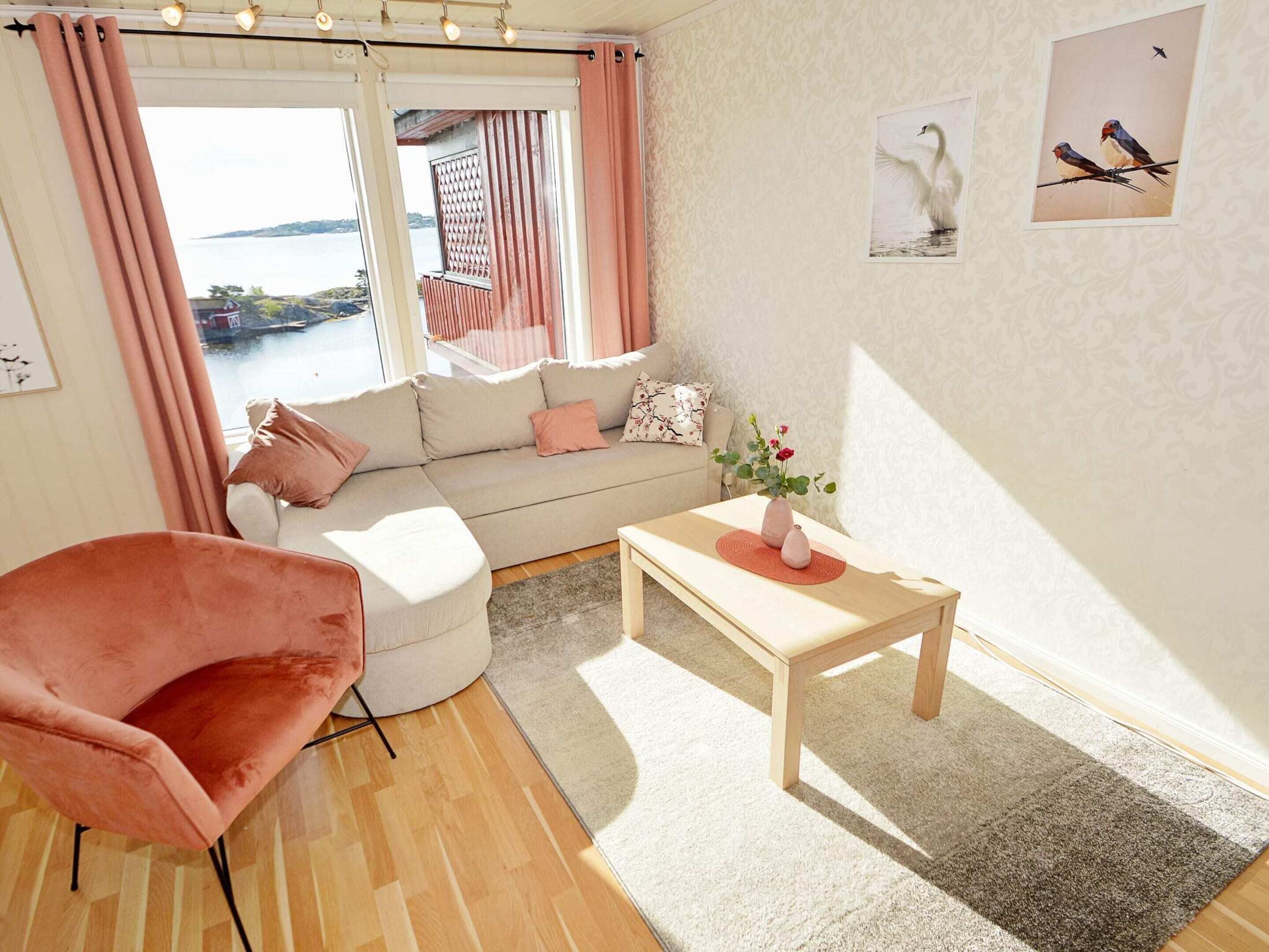 Un salon moderne avec un canapé, un fauteuil rose, une table en bois et une vue sur la mer.