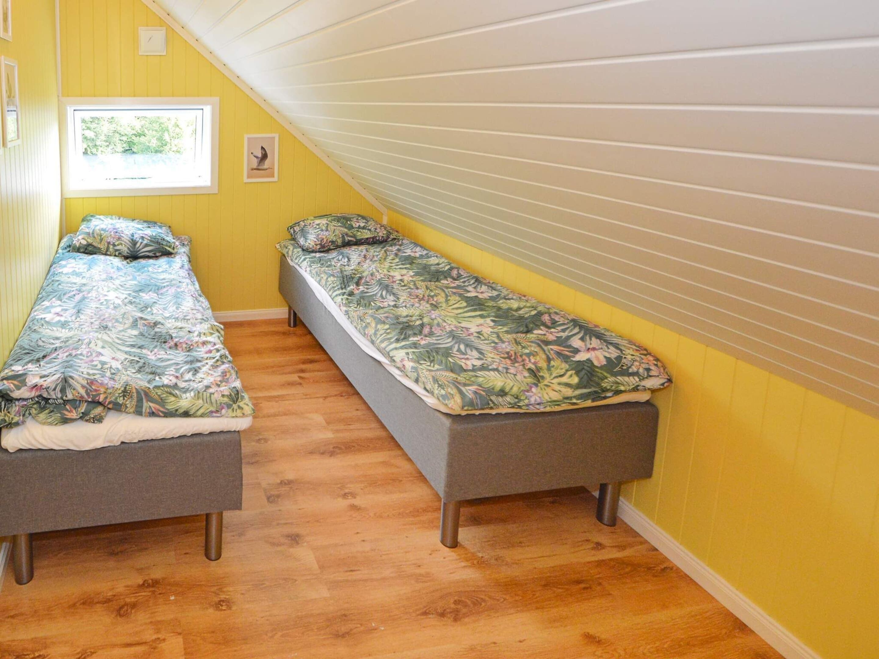 Una habitación con dos camas individuales, suelo de madera, techo inclinado y ventana con vistas.