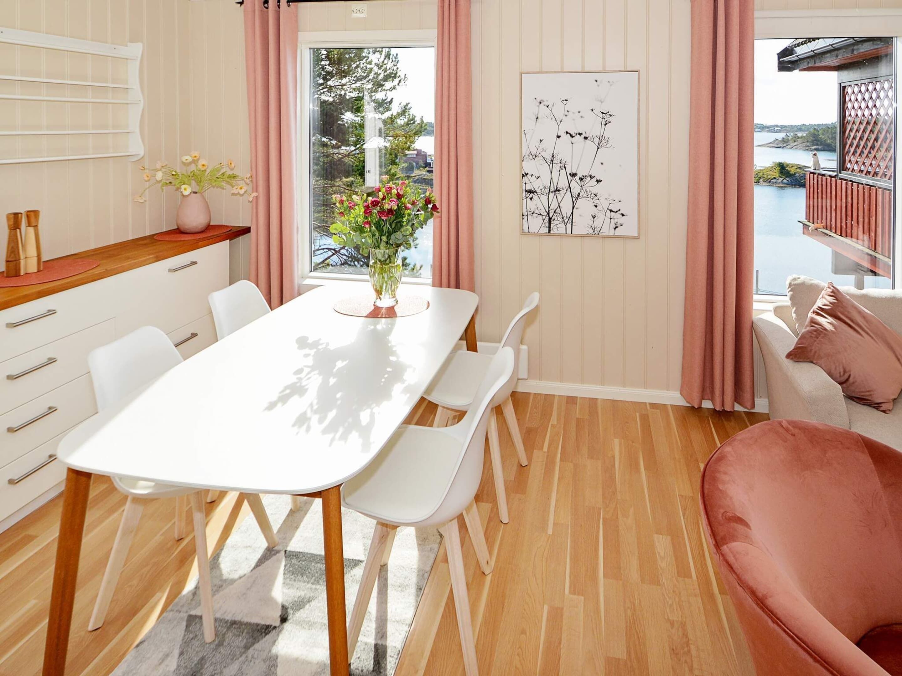 A modern dining area with a white table, white chairs, and a vase of flowers.