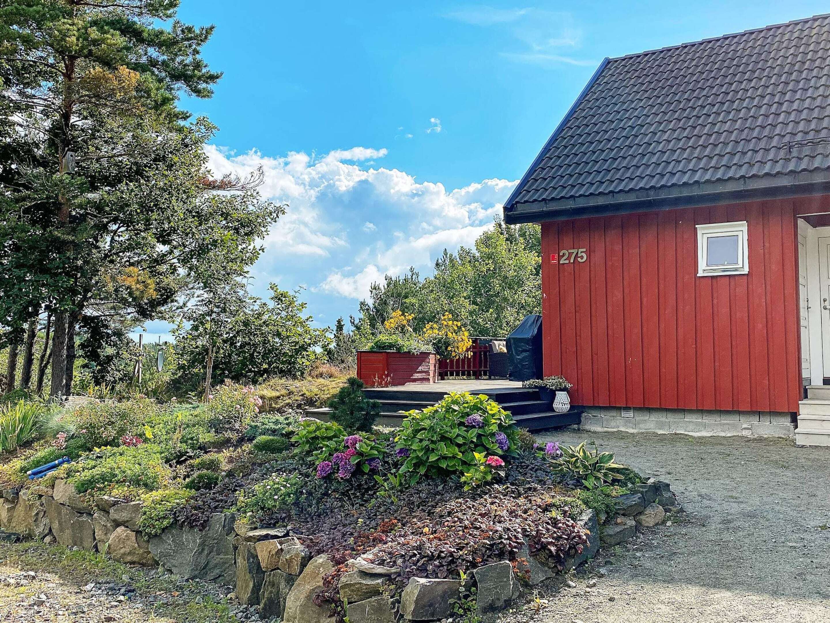 A red building with a number '275' on the side, surrounded by a garden with various plants and flowers.