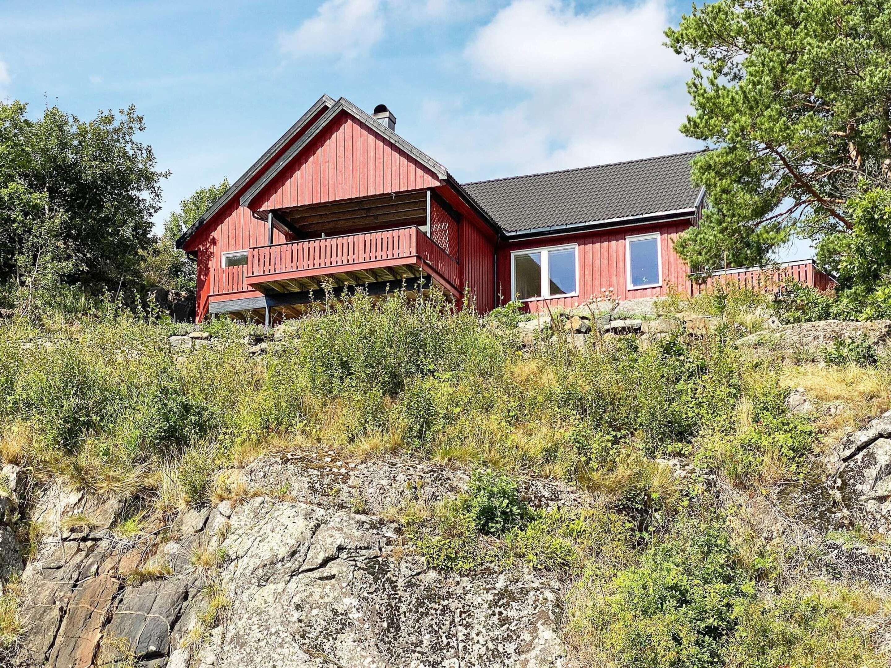 Una casa de madera roja con balcón, rodeada de vegetación natural y rocas.