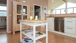 A kitchen with wooden cabinets, a white cart with books, and a dishwasher.
