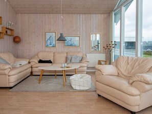 A living room with a beige sofa set, a round coffee table, and a white pouf.