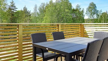 An outdoor deck with a table and chairs, surrounded by a wooden fence and trees.