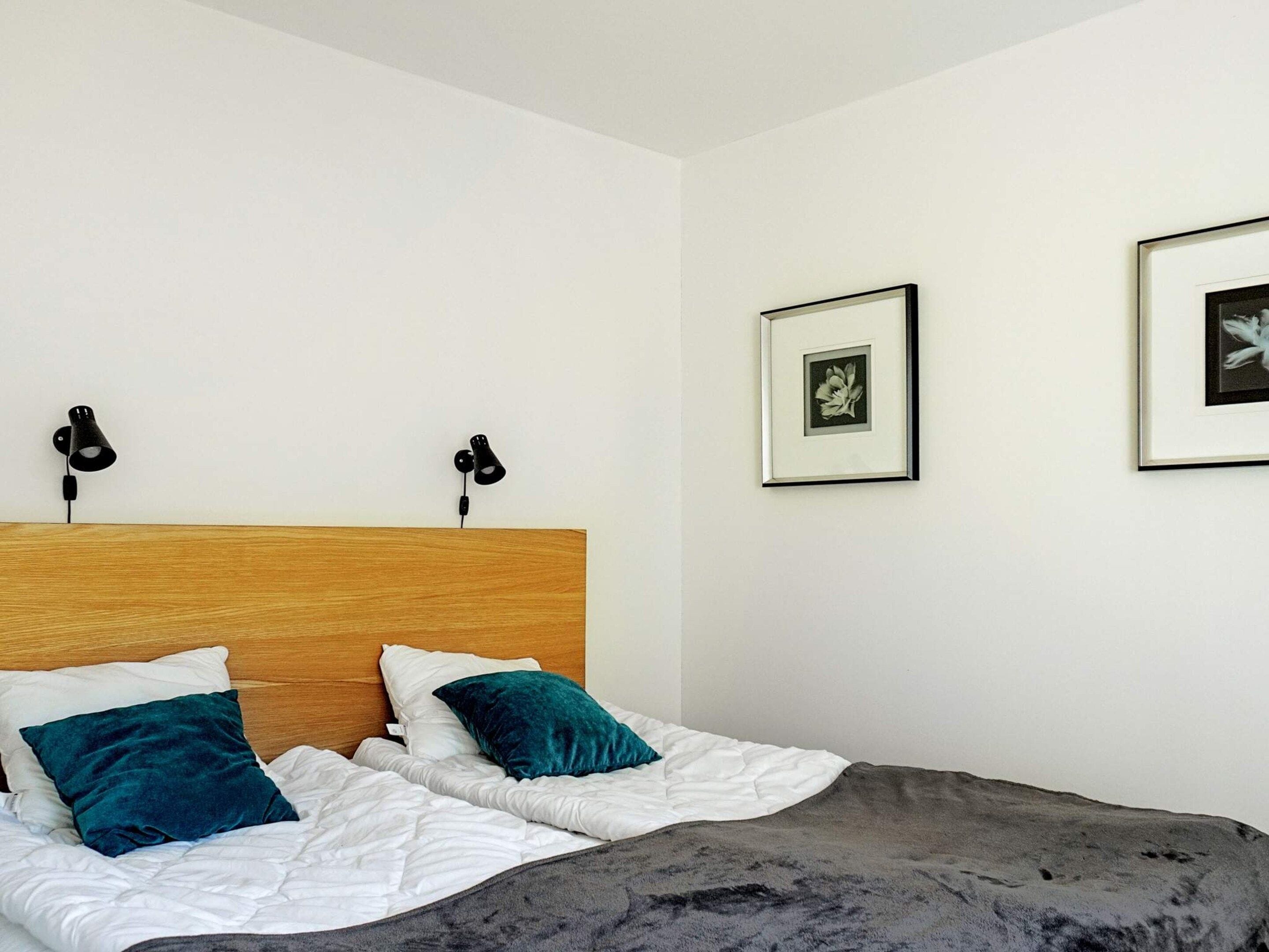 Quarto com cabeceira de madeira, duas almofadas, um cobertor e duas luminárias na parede.
