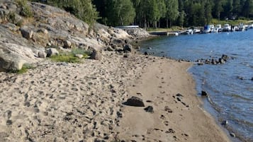 A sandy beach with visible footprints, a rocky shoreline, and boats in the water.