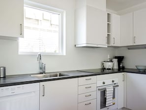 A modern kitchen with white cabinetry, a stainless steel sink, a window with blinds, and a built-in oven. - 5 Person Holiday Home in Stromstad (Stromstad)