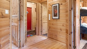 A wooden cabin interior with a hallway leading to a red door, a framed artwork on the wall, and a bunk bed in the corner. - Holiday Home in Tonstad (Sirdal)