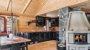 A cozy cabin interior with a stone fireplace, wooden floors, and a kitchen with black cabinets. - Holiday Home in Tonstad (Sirdal)