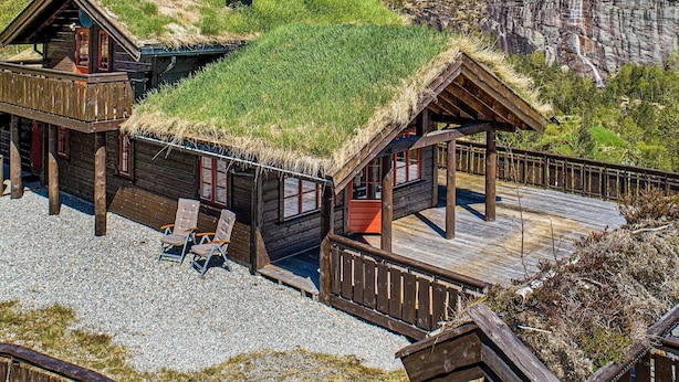 A cabin with a thatched roof, wooden deck, and a view of a waterfall. - Holiday Home in Tonstad (Sirdal)