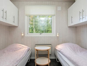 Two single beds with light-colored bedding, a small table, and a wall-mounted heater.