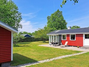 Une maison rouge avec un patio couvert, une pelouse et une haie.