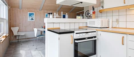Una cocina moderna con armarios blancos, horno empotrado, microondas y techo de madera.
